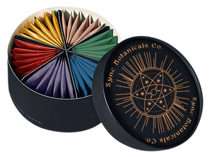 Open Sync Botanicals monthly tea box showing six color coded wedges of tea bags, with the black and gold lid beside it.